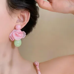Nahaufnahme von Ohrringen mit rosa Chiffonblumen und Harz-Tropfenanhängern an einem Modell.