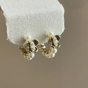 Close-up of vintage butterfly earrings with pearls and crystals on beige fabric backdrop.
