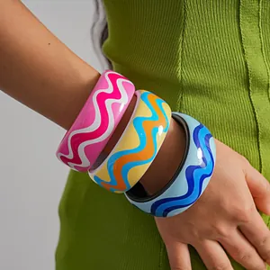 Detailed view of three colorful resin bangles with vibrant wavy print on a model's arm