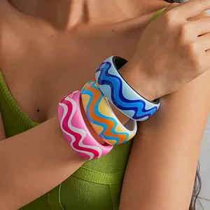 Detailed close-up of vibrant colorful wavy pattern resin bangles worn on a fashion model's arm.