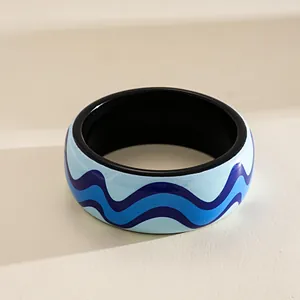 Macro shot of a glossy resin bangle featuring a vibrant blue wavy ocean pattern.