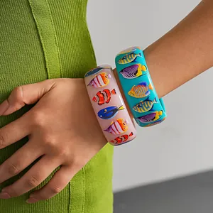 Detailed view of glossy resin bangles featuring colorful tropical fish prints on a woman's wrist