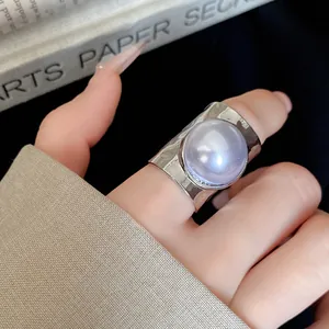 Close-up view of a large purple pearl set in a wide silver open band ring on a finger.