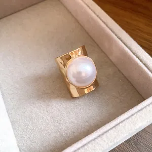 Close-up of a wide gold band ring featuring a large white pearl in a jewelry box