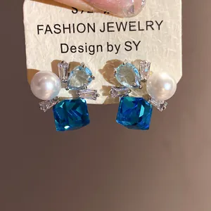 Macro detail of retro zircon and pearl stud earrings with blue square crystals