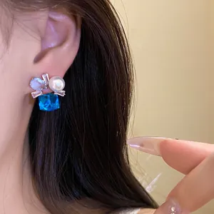 Close-up of elegant stud earring with blue zircon, pearl and clear crystals on model's ear