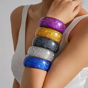 Detail shot of colorful resin bangles with glitter stars and snowflakes on a model's arm.