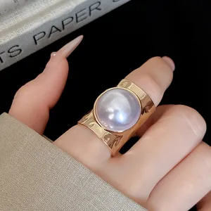 Close-up of a large iridescent pearl set in a wide gold-colored open ring band.