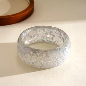 Close-up detail of a clear resin bangle featuring embedded silver stars and snowflake glitter.