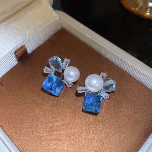 Close-up of vintage-style blue zircon and pearl stud earrings in a jewelry box.