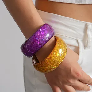 Macro detail of colorful chunky resin bangles with embedded stars and glitter on a model wrist.