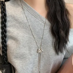 Vue détaillée d'un collier à pampilles en forme de fleur sur un haut en maille grise chic.