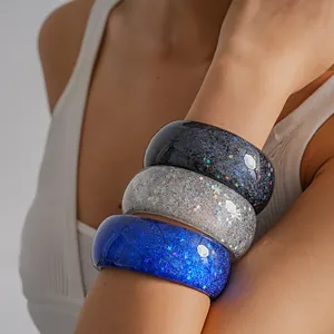 Close-up of three sparkling resin bangles with star and glitter patterns on a wrist.