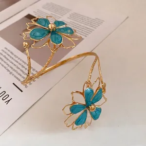 Gold metal arm cuff bracelet with blue enamel flowers in vintage luxury style.