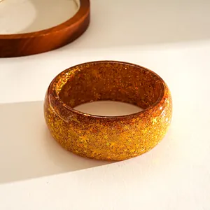 Macro detail of a translucent amber resin bangle embedded with golden star-shaped sequins