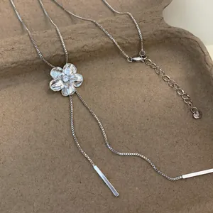 Gros plan d'un pendentif fleur argenté serti de cristaux sur un collier à pampilles en maille