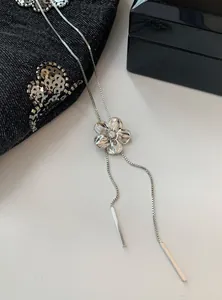Détail en gros plan montrant la fleur en argent et le strass de ce collier à pompons
