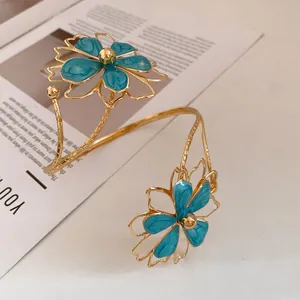 Detail shot of a gold-tone metal arm cuff with turquoise enameled flower motifs.