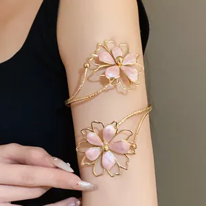 Close-up of gold metal arm cuff featuring delicate pink enamel flowers on model arm
