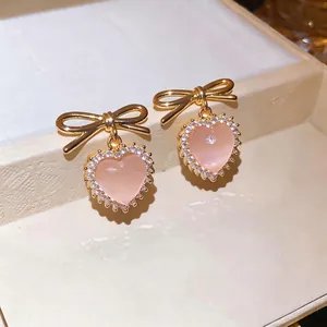 Sweet pink cat's eye heart stud earrings featuring a golden bow and sparkling crystal trim