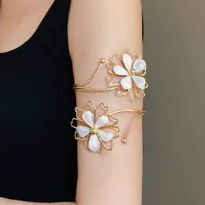 Detail view of a gold-finish arm cuff featuring elegant white enamel flowers decoration