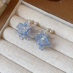 Macro detail of light blue translucent flower stud earrings with pearls in a box