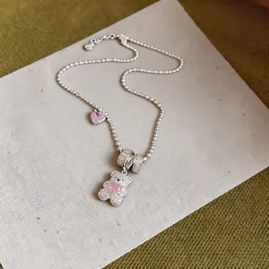 Close-up of a delicate silver necklace featuring a sparkling bear and pink heart.