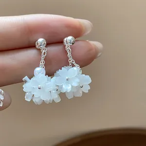 Close-up of elegant silver earrings with white cherry blossom petals and pearl accents.