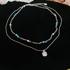 Close-up of a double-layer silver necklace with blue beads and a square zircon pendant.
