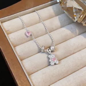 Detail showing a silver bead chain necklace with pavé zircon bear and heart pendant