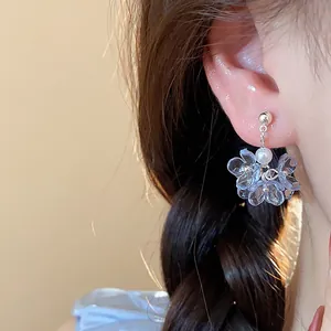 Close-up detail view of light blue resin flower earrings with a white pearl on an ear