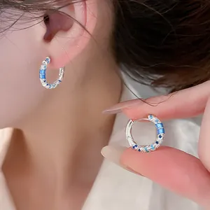 Close-up of silver hoop earrings with blue enamel patterns being worn and held