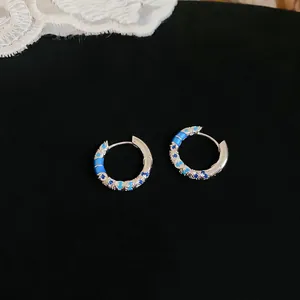 Macro detail view of elegant silver hoop earrings with blue zircon and enamel pattern.