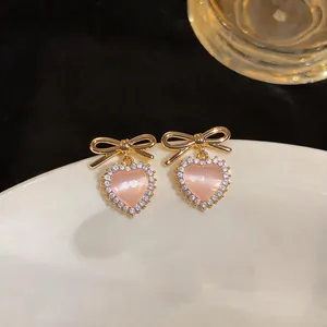 Detailed view of pink cat-eye heart earrings with golden bow studs and crystals