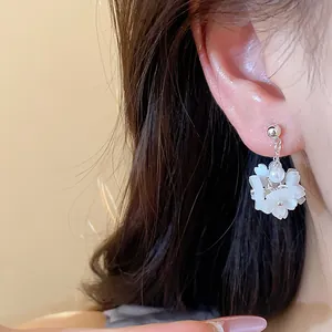 Close-up detail of elegant white floral pearl stud earrings worn on a person's ear