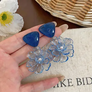 Close-up of transparent blue resin flower earrings with delicate central pearl detail