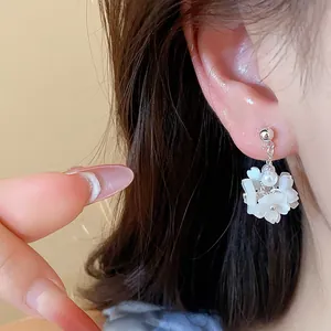 Close-up detail of a delicate white flower and pearl drop earring worn on the model's ear