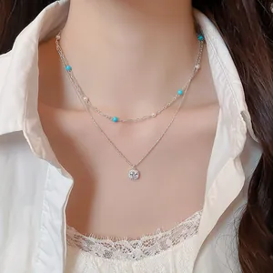 Detail shot of layered silver-toned necklace with blue beads and square zircon pendant