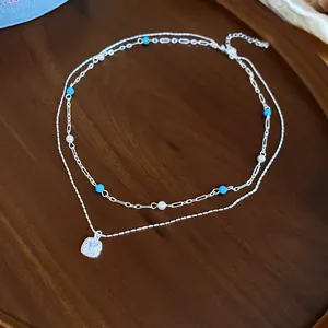 Detailed view of a double layered silver necklace with blue beads and a zircon stone