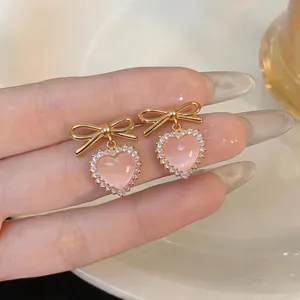 Close-up of pink heart cat-eye stone earrings with gold bow-knot and rhinestones