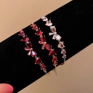 Detailed close-up of zircon bow and heart bracelets in red and pink on a black display.