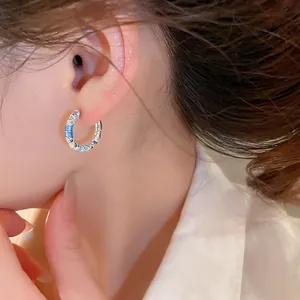 Detail of silver hoop earring with blue enamel and zircon worn by a model.