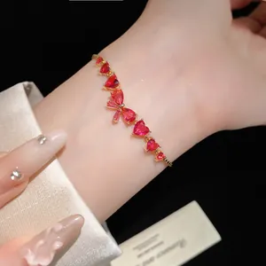 Detailed view of a gold-tone zircon bracelet with red heart and bow-knot charms