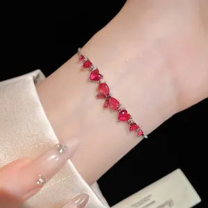 Detailed view of a bow and heart-shaped red zircon bracelet on a woman's wrist.