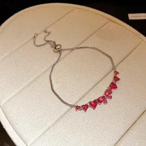 Detail view of a silver bracelet featuring pink heart and drop zircon bow charms.
