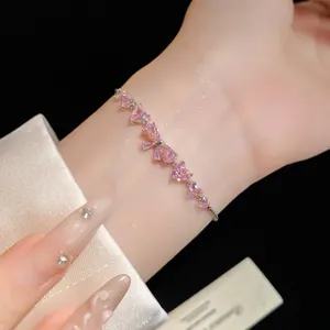 Close-up of elegant pink zircon bow and heart bracelet on wrist with silk background