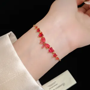 Close-up of a delicate red zircon bow and heart bracelet with a golden finish on the wrist