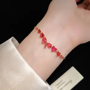 Close-up view of an elegant red zircon heart and bow bracelet worn on a person's wrist.