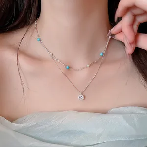 Detailed shot of a double-layer silver necklace with blue beads and a square zircon pendant