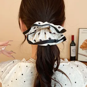 Detailed view of a French style white and black polka dot scrunchie on a ponytail